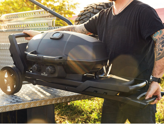 Portable grill being loaded into a pickup truck, illustrating ease of transport for tailgating or outdoor events. The image highlights the compact grill being placed in the truck bed, ideal for convenient grilling on the go.